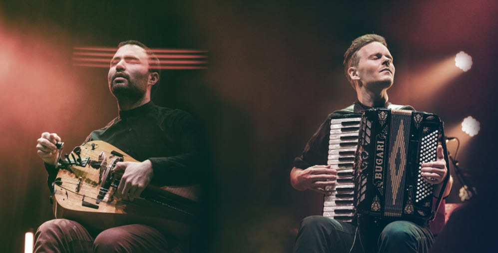 Två personer sitter på en sen och spelar varsitt instrument och tittar ut över publiken
