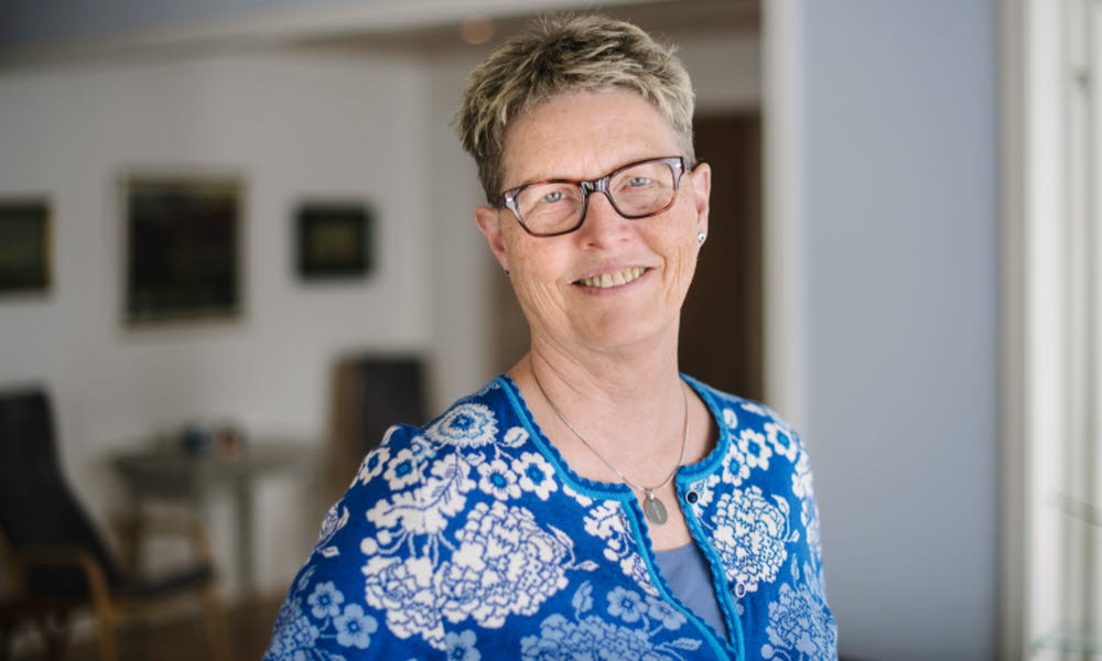 AnnKatrin Norelius, medelålders kvinna med kort blont hår, ler mot kameran. Halvbild, hon bär en blå mönstrad tröja.