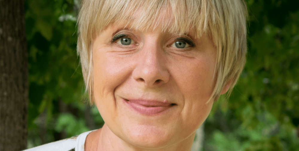 En kvinna med blont hår ler mot kameran.