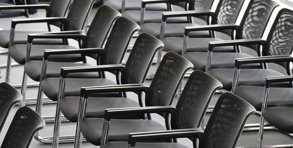 Rader av tomma svarta stolar i ett konferensrum.