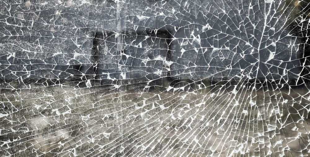 Närbild av ett splitterkrossat fönster med spindelnätsliknande sprickmönster.