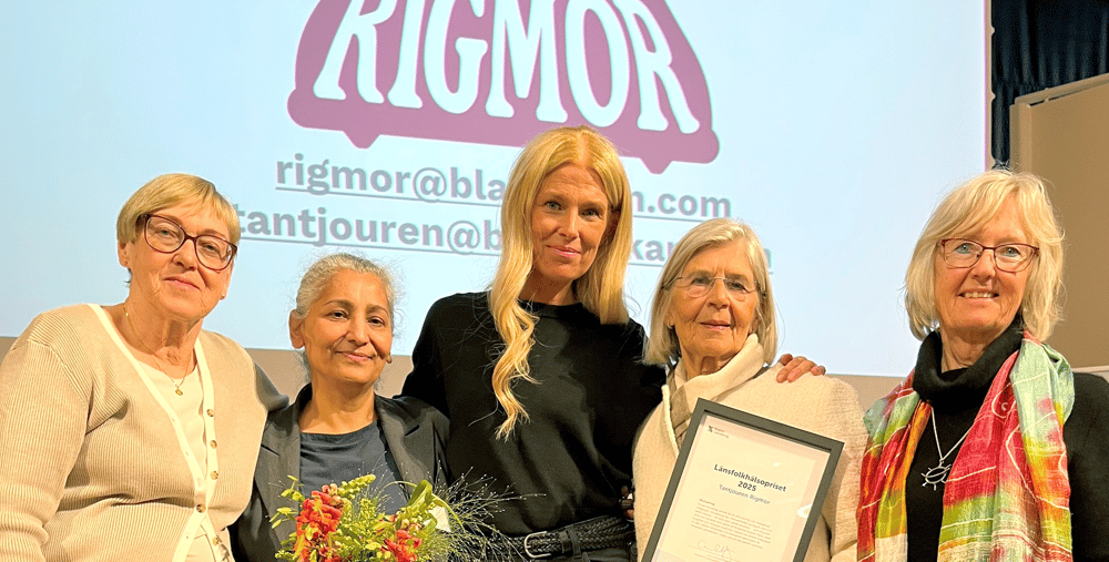 Fem personer i halvfigur står framför en skärm med ordet Rigmor. De har blommor och diplom i händerna