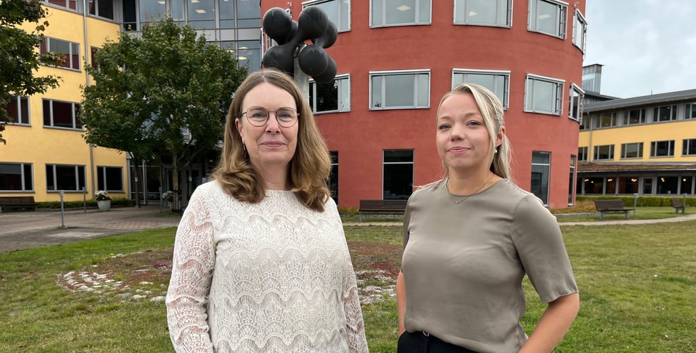 Två kvinnor i halvfigur framför en stor byggnad.