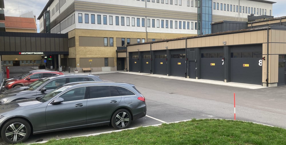 Hus 07/08 på Hudiksvalls sjukhus. I förgrunden syns portarna till ambulansintaget och i bakgrunden syns ingången till akutmottagningen. Bilar är parkerade i förgrunden. 