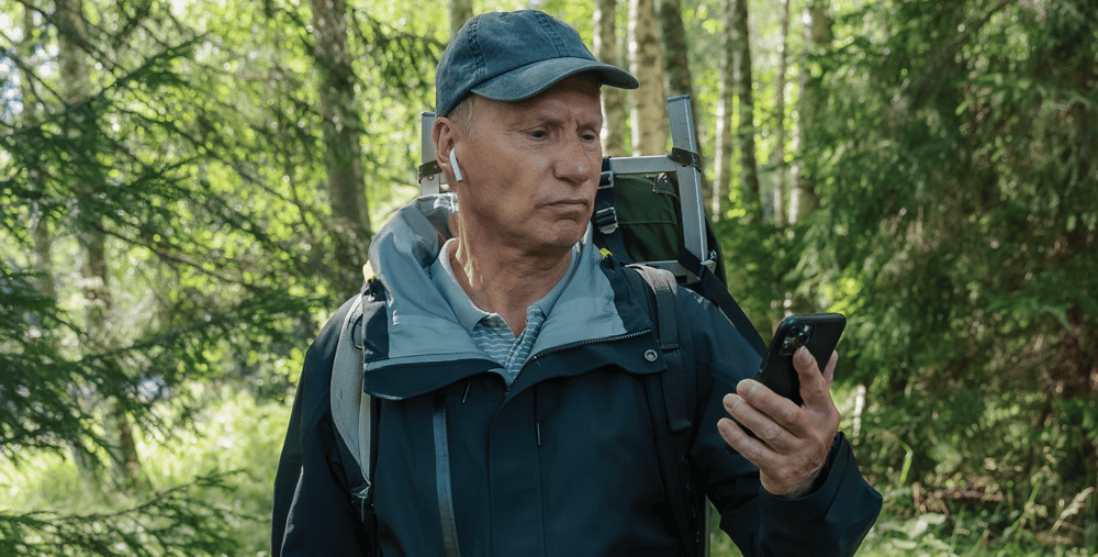 En man som står i skogen och tittar på sin mobiltelefon.