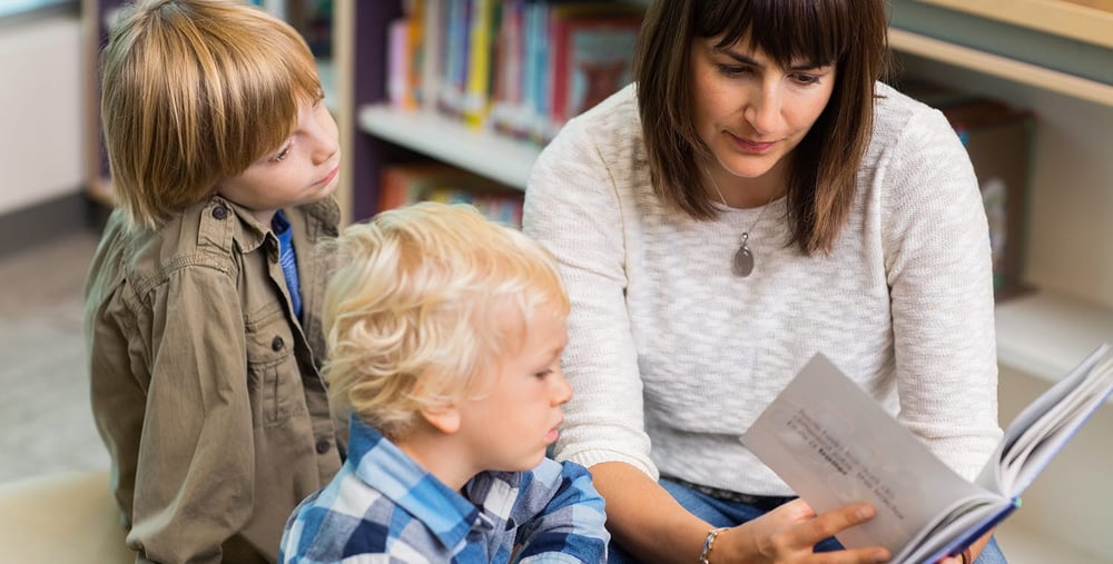 Young teacher reading book for students in school library