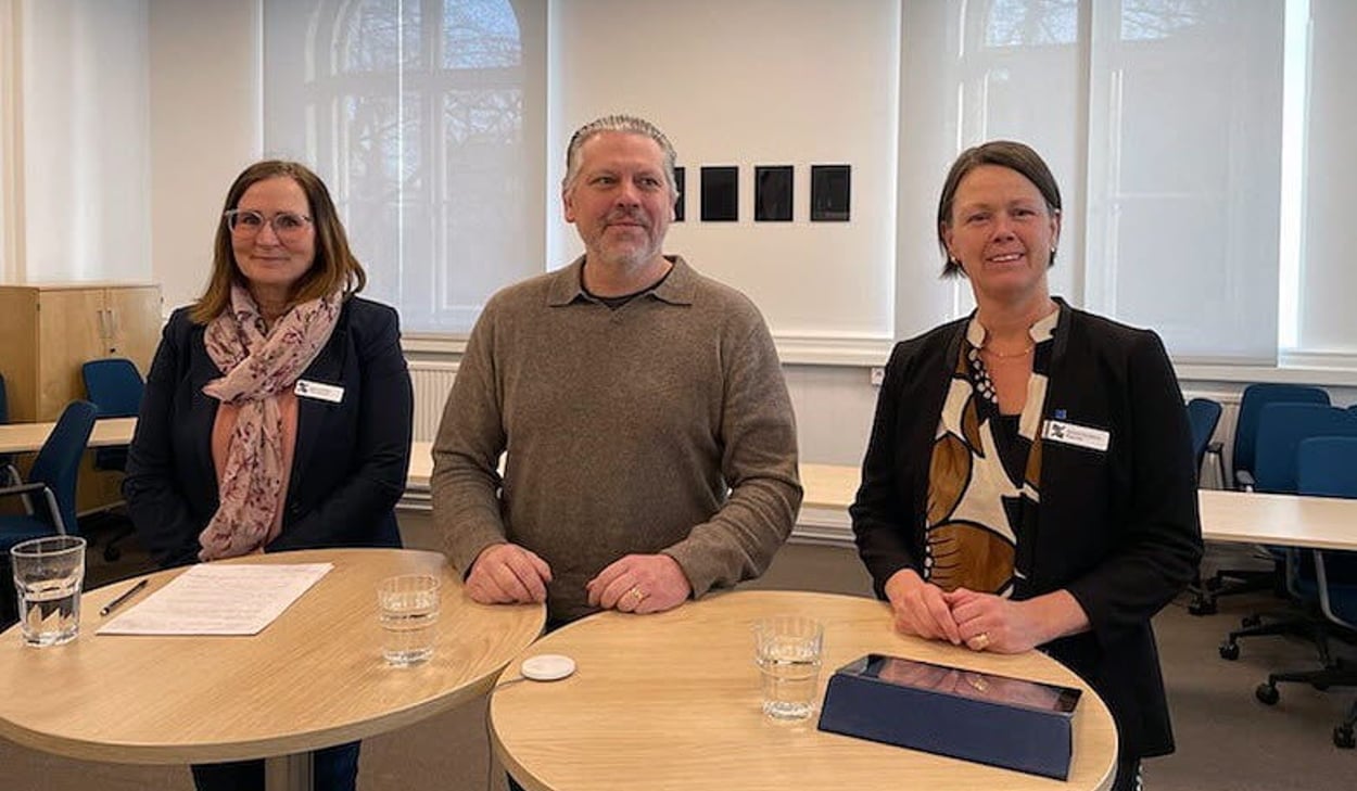 Tre personer står bakom höga ståbord. 