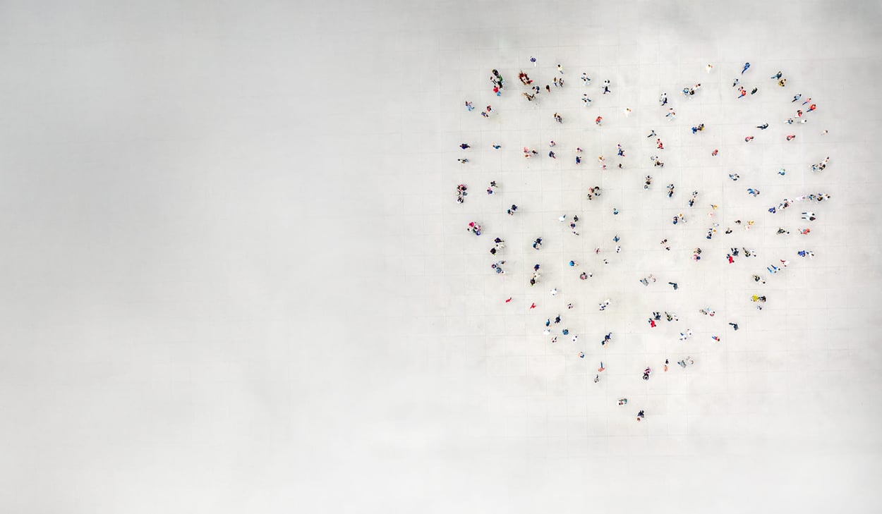Människor står utspridda så att de tillsammans bildar formen av ett hjärta på en stor öppen yta, sedd uppifrån.