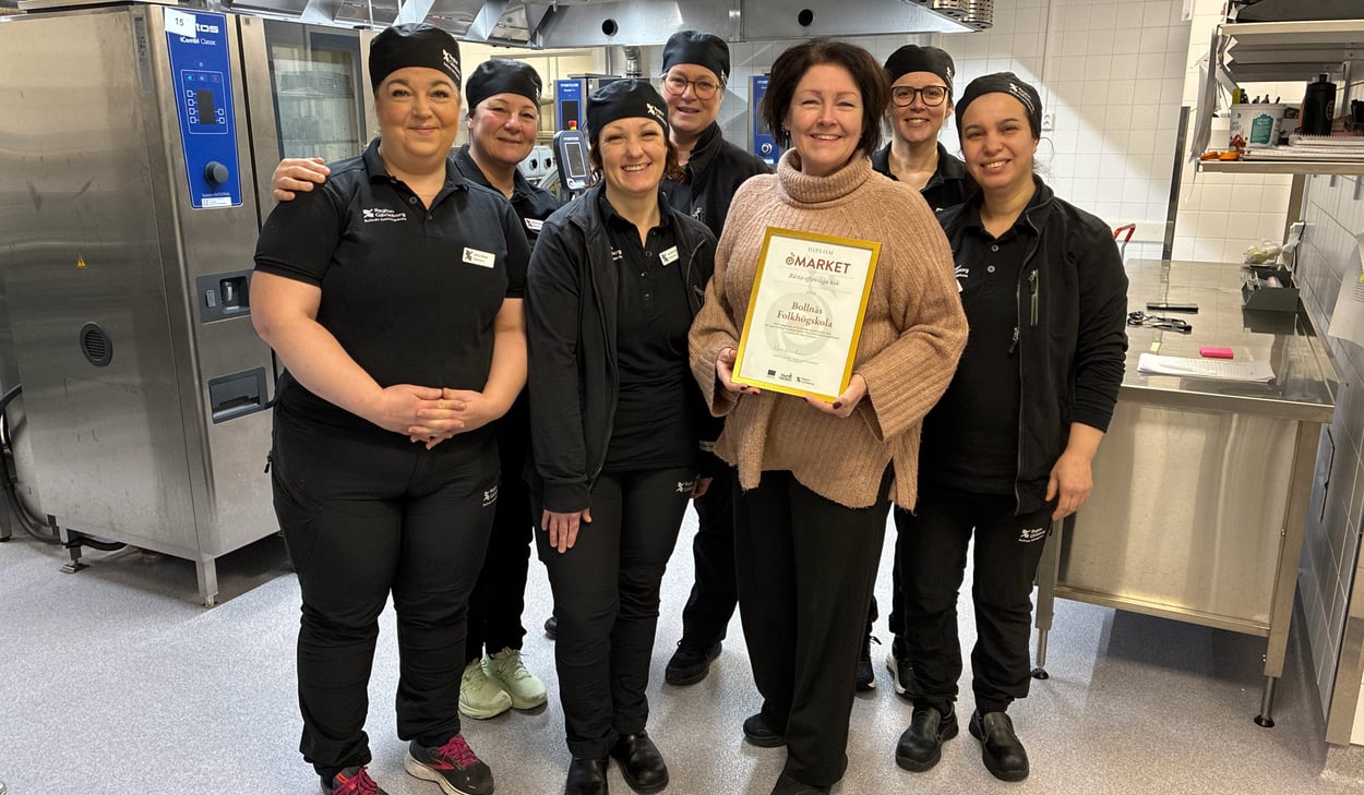 Sju personer står uppradade bredvid varandra i ett stort restaurangkök. 