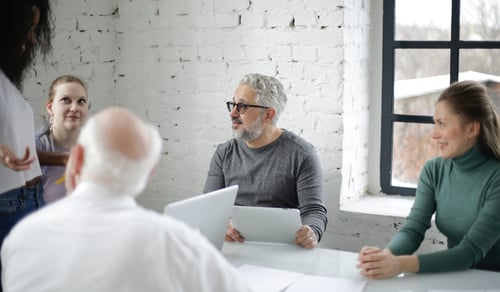 Fem personer i olika åldrar runt ett mötesbord.