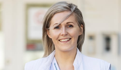 En kvinna i vårdkläder ler mot kameran.