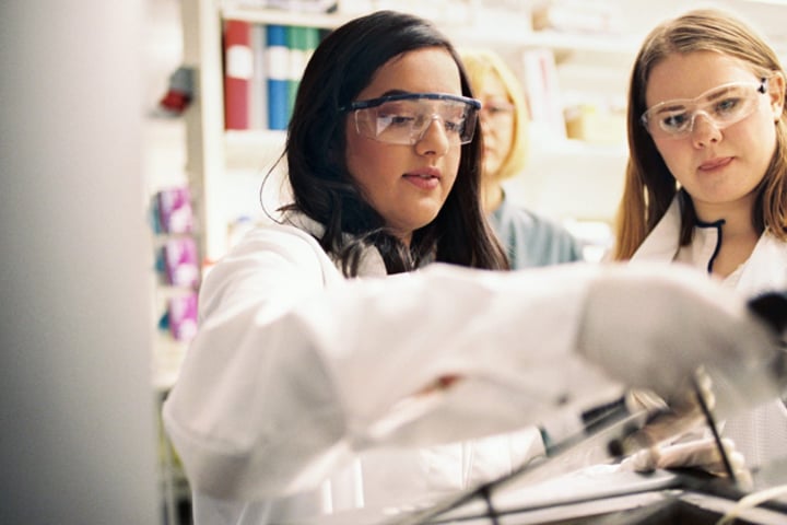 Två kvinnor i labbrockar tittar på en datorskärm.