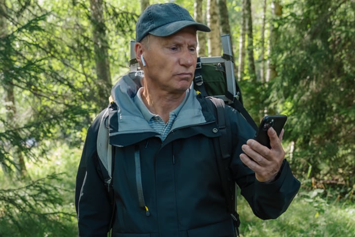 En man som står i skogen och tittar på sin mobiltelefon.