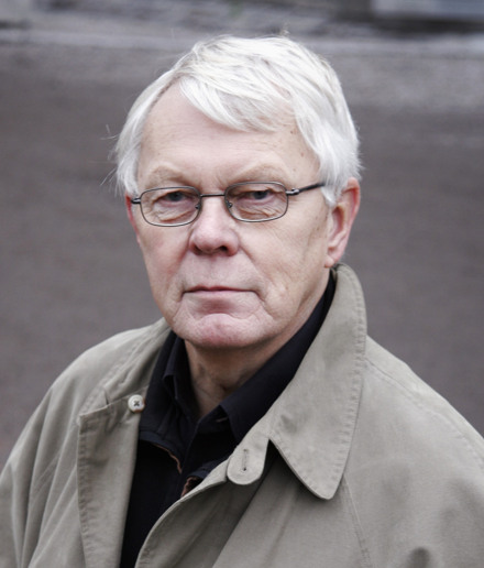 En man med vitt hår som bär en trenchcoat.