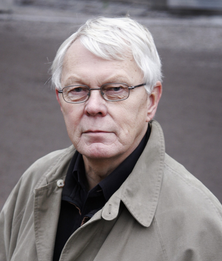 En man med vitt hår som bär en trenchcoat.