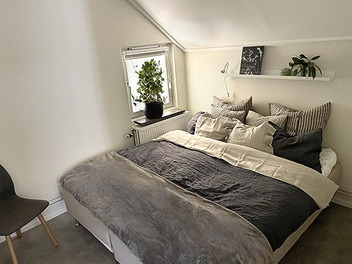 En s&auml;ng som st&aring;r i ett sovrum bredvid ett f&ouml;nster.