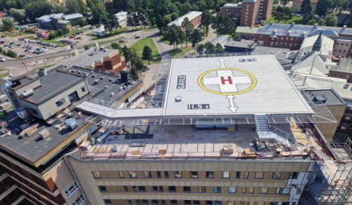 Bilden visar den nya helikopterplattan på taket av hus 60. Helikopterplattan är fortfarande en byggarbetsplats. Bilden visar också en del av den ny tillbyggnaden av 6 våningar och den nya fasaden på den södra sidan av byggnaden.