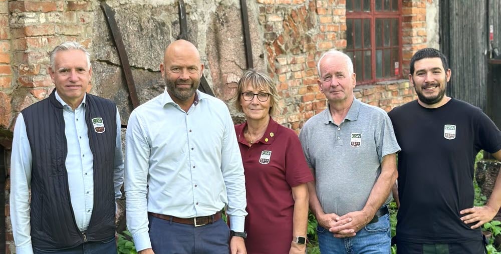 Fem personer står i helkroppsfigur framför en gammal tegelbyggnad.