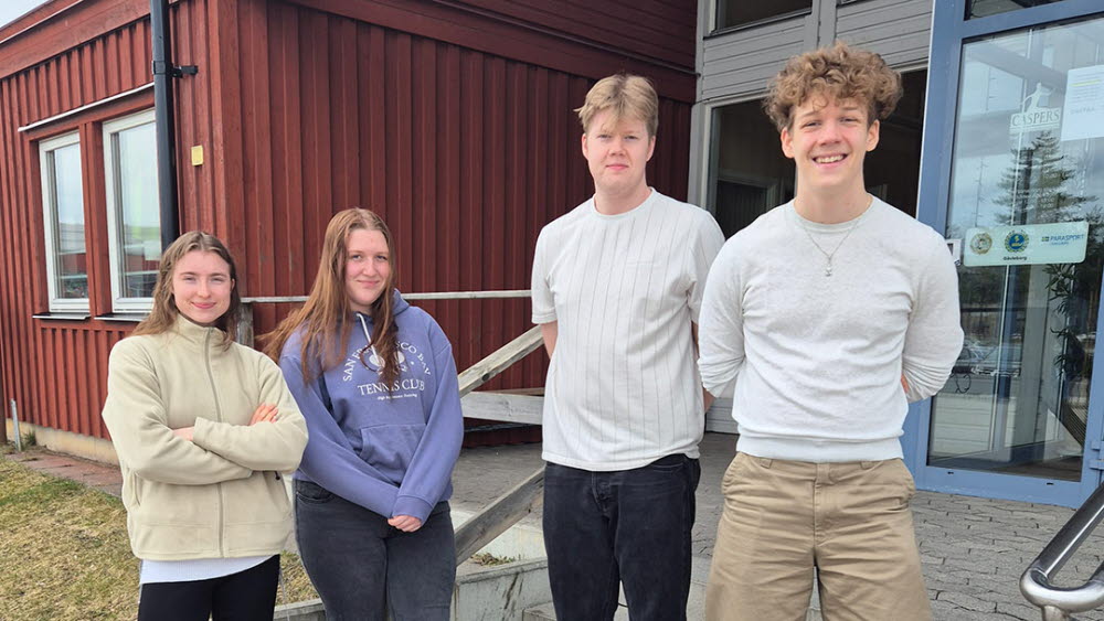 Fyra personer ståendes utanför en röd byggnad med blå glasdörr.