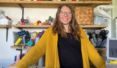 Person som står framför hyllor med tyger och vävverktyg