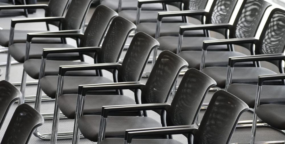 Rader av tomma svarta stolar i ett konferensrum.
